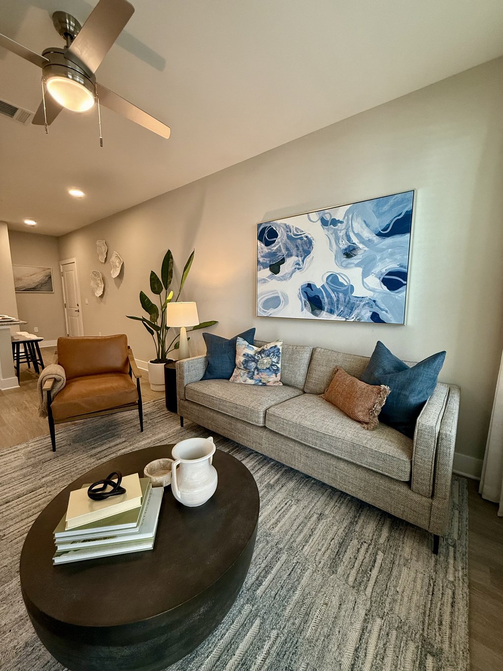 A living room with a grey couch, a brown armchair, a coffee table, and a large blue and white painting on the wall.