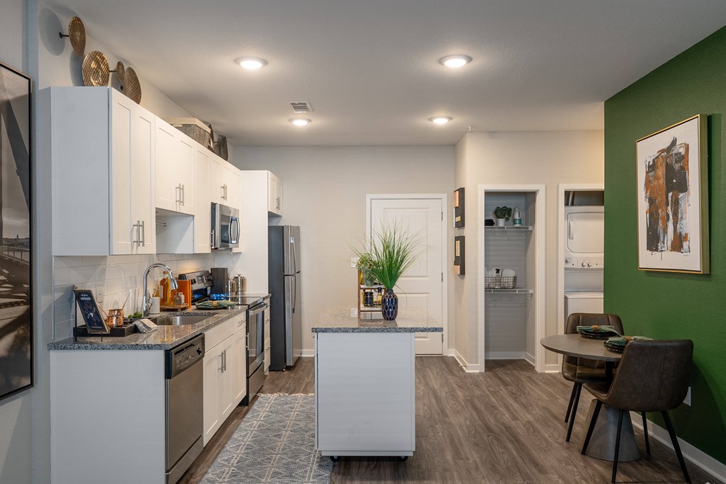 a kitchen and dining room with white cabinets and stainless steel appliances and a green wall