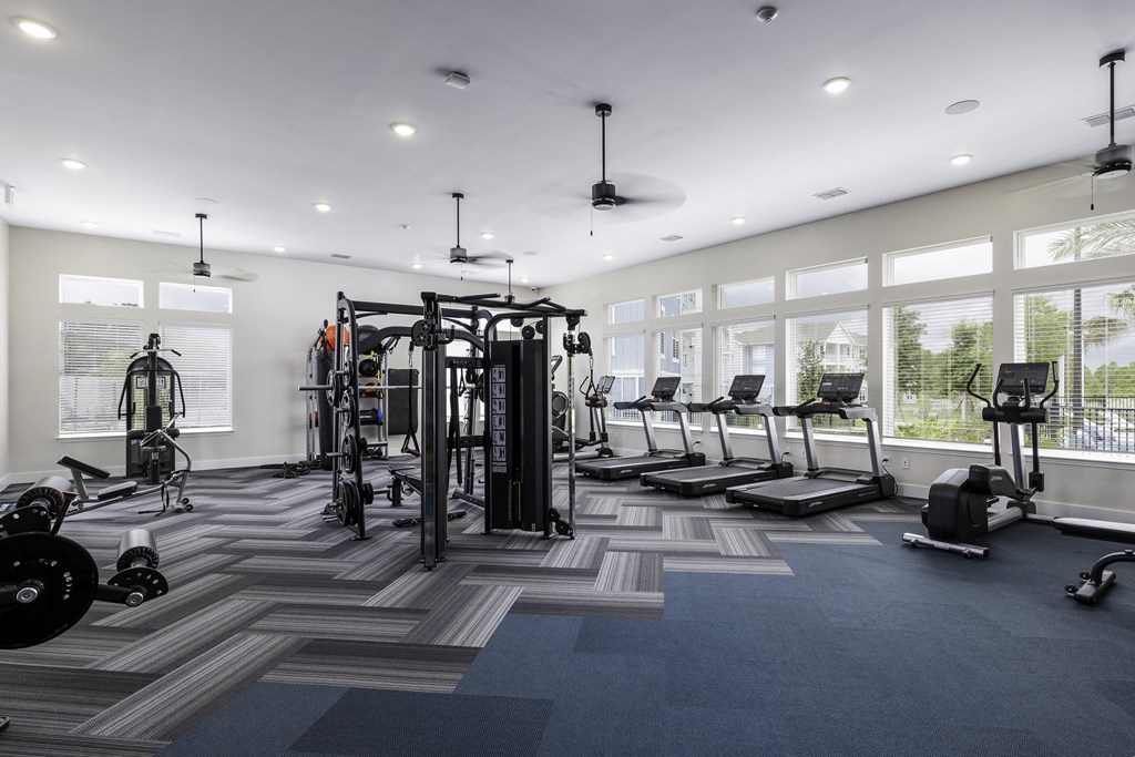 a gym with weights and cardio equipment in a building with large windows