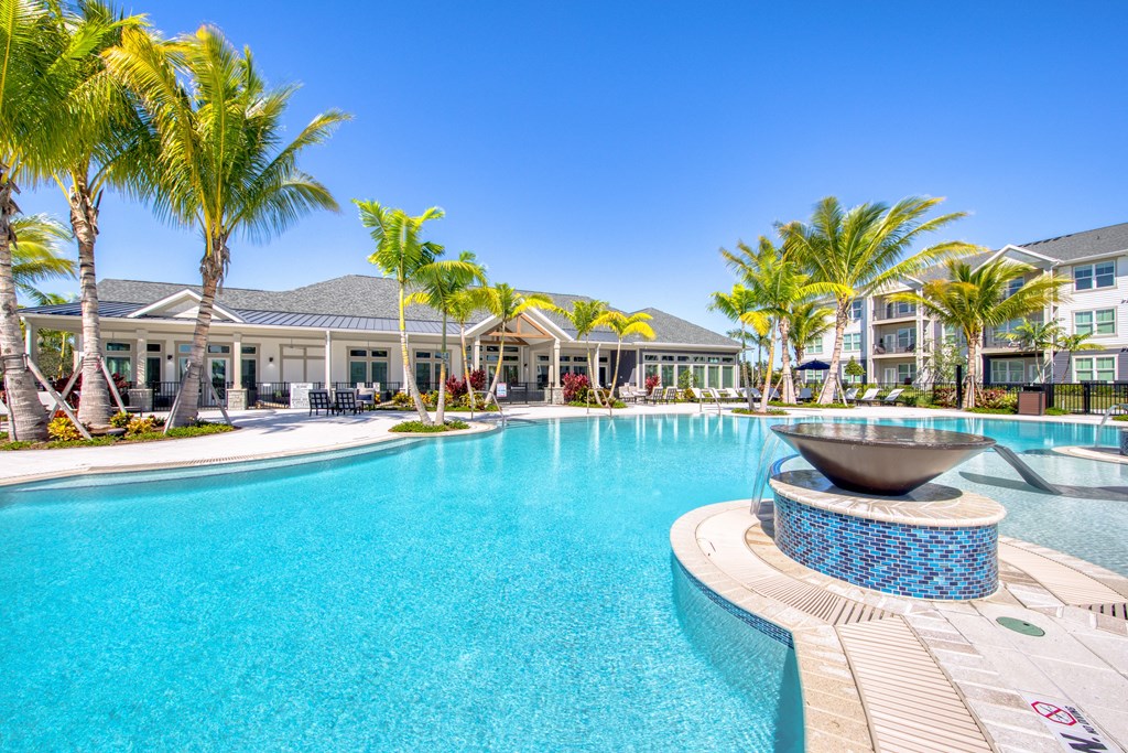 a large swimming pool with palm trees and a building in the background