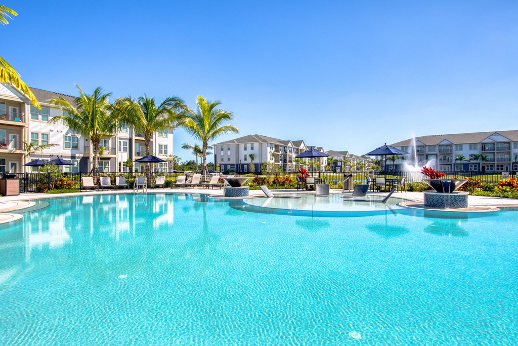 a large swimming pool with palm trees and buildings in the background