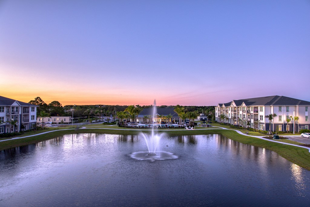 a fountain in the middle of a pond at sunset