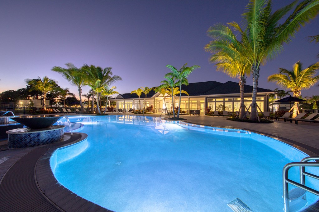a swimming pool at night with palm trees and a building in the background