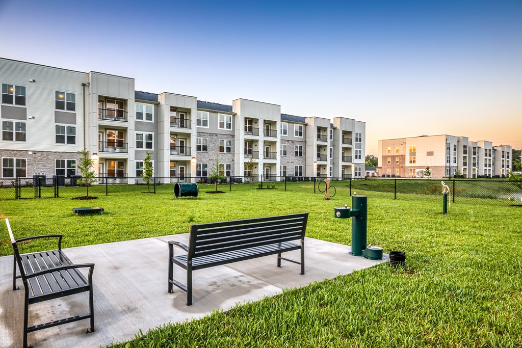 A park with benches and grass in front of apartment buildings.