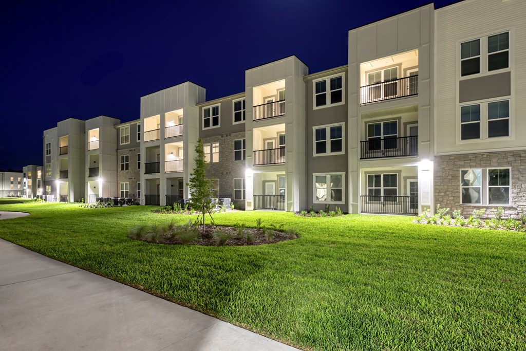 Apartment complex with green lawn and lights on.