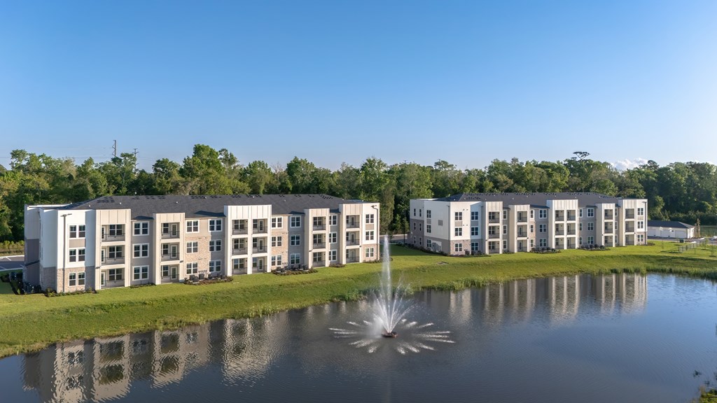 A fountain in the middle of a pond in front of a building.