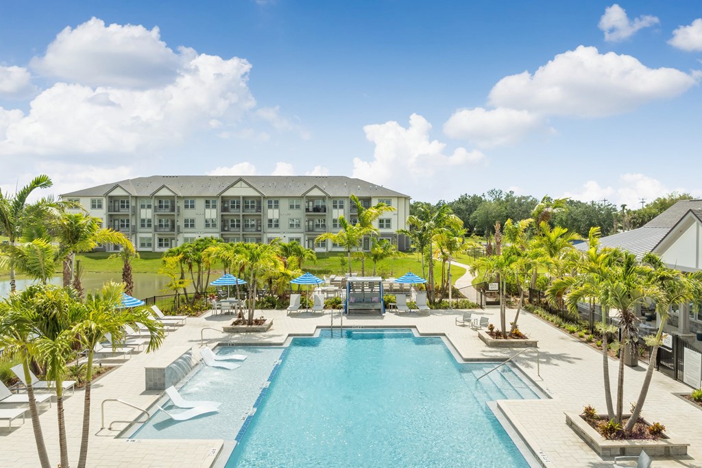 a large swimming pool with palm trees and a building in the background