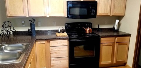 A black stove top oven sits in a kitchen with wooden cabinets.