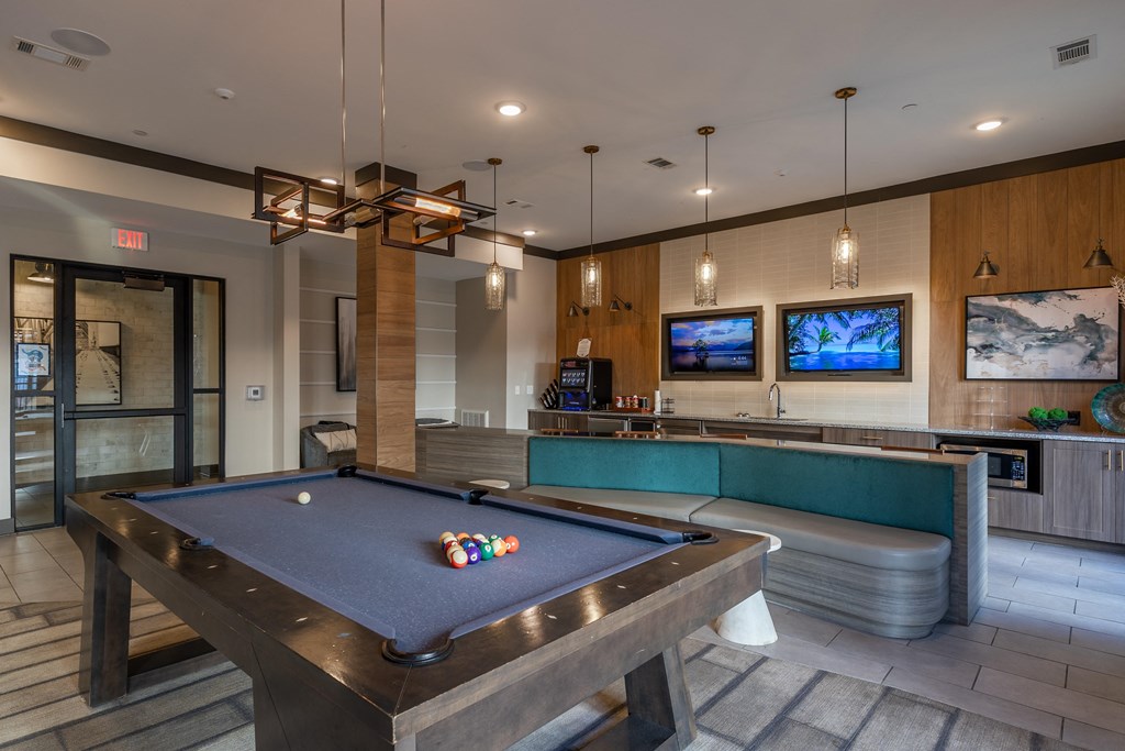 a pool table in a clubhouse with a bar and tv