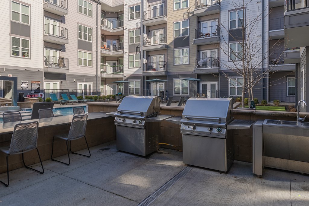 a group of stainless steel barbecue grills in an outdoor patio with an apartment building