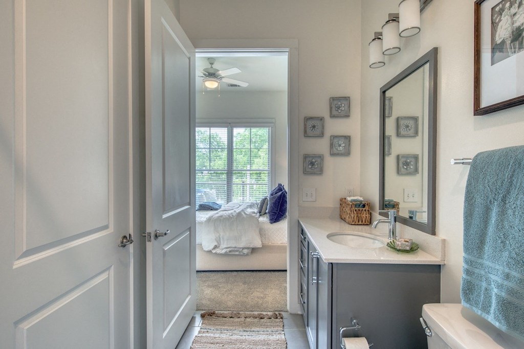 a bathroom with a sink and a mirror and a door to a bedroom