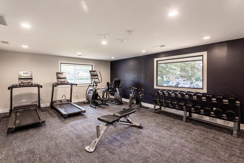 a gym with cardio equipment and weights in a room with a window