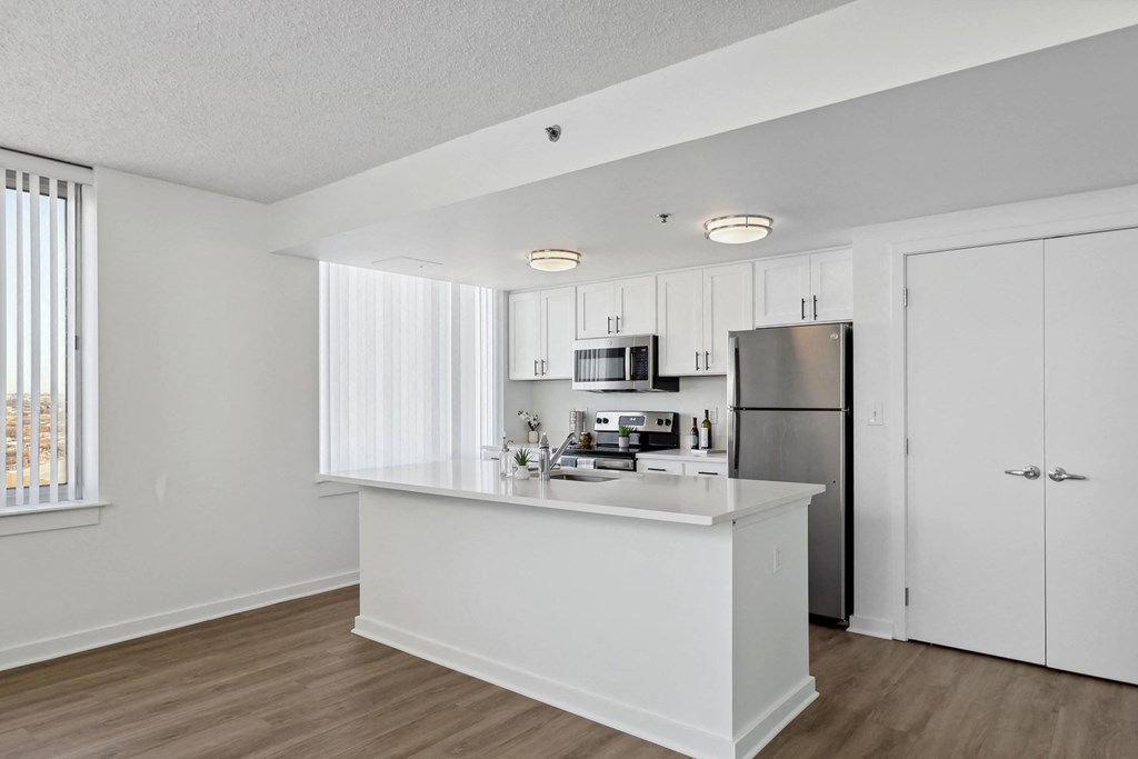 a white kitchen with a large island and stainless steel refrigerator at The Zenith, Baltimore, MD, 21201