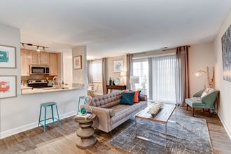 a living room with a couch coffee table and chairs and a kitchen in the background