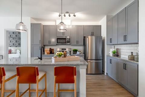 a kitchen with stainless steel appliances and a counter with three orange chairs