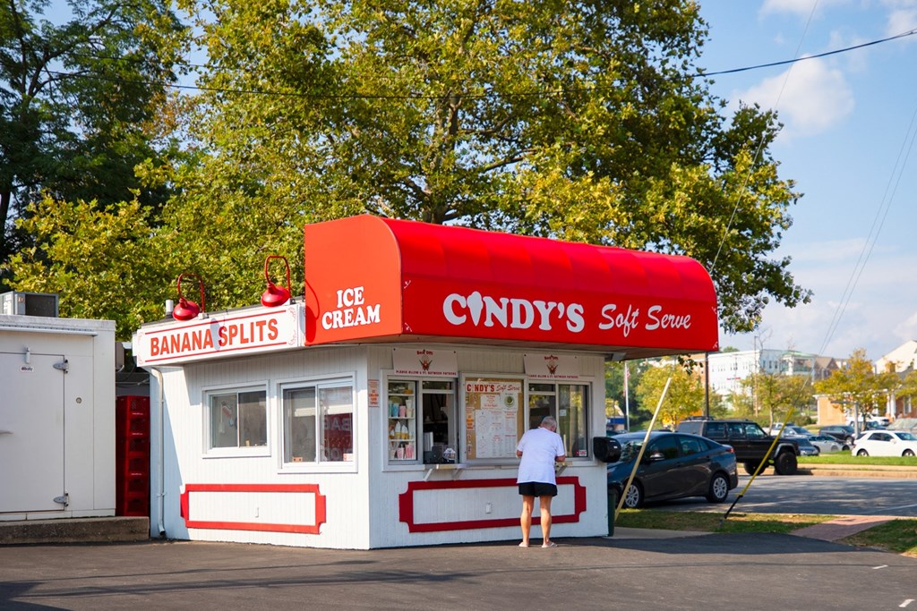 a woman stands at the counter of a white and red ice cream shop with a red roof