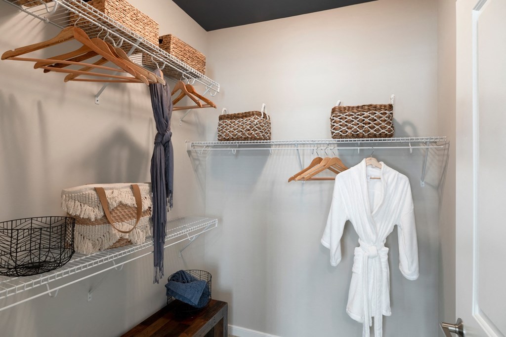 a walk in closet with shelves and baskets and a white robe hanging on the wall