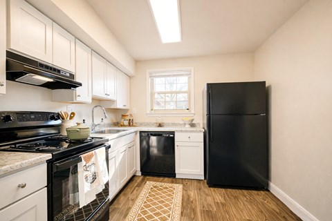 A black refrigerator stands in a kitchen with white cabinets and a black stove.