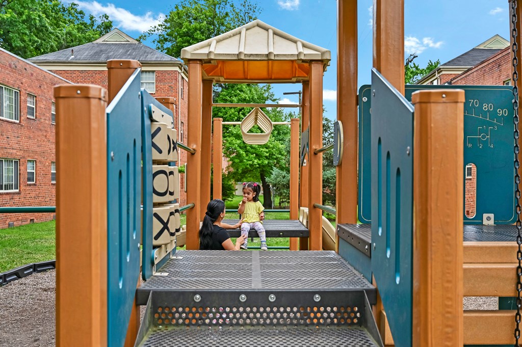 a woman and a child sitting on a swing on a playground at Hamilton Manor Apartments, Hyattsville