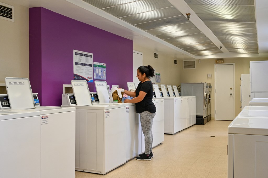 a woman standing at a line of washing machines in a laundromat at Hamilton Manor Apartments, Hyattsville, MD