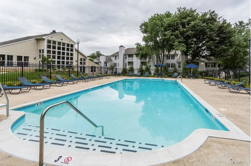 a swimming pool with chaise lounge chairs and apartment buildings in the background at Madison at Eden Brook, Columbia, MD