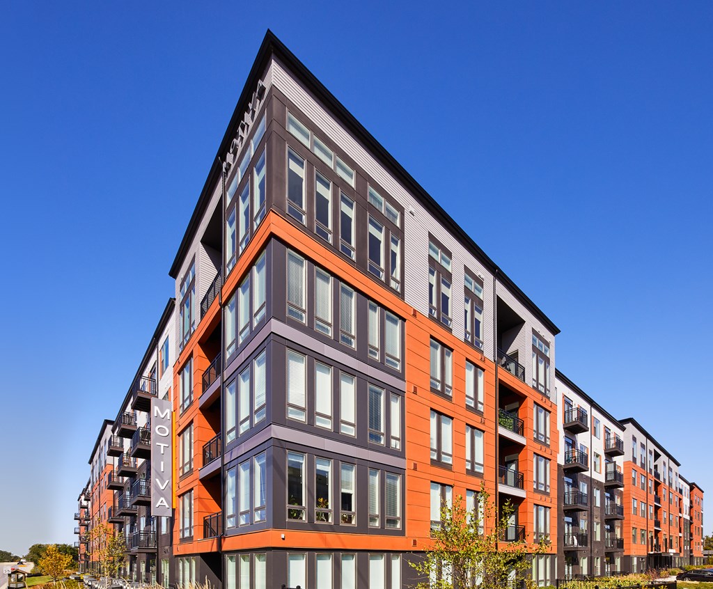 A modern multi-story building with balconies and a clear blue sky in the background.
