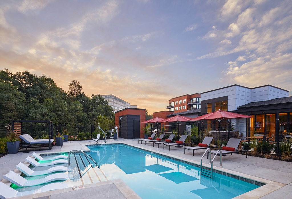 A swimming pool with red umbrellas and lounge chairs.