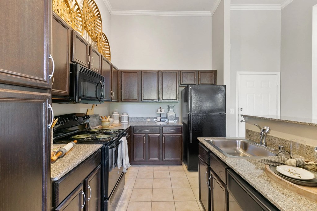 A kitchen with black appliances and brown cabinets at Prairie Crossing, Farmers Branch, 75244