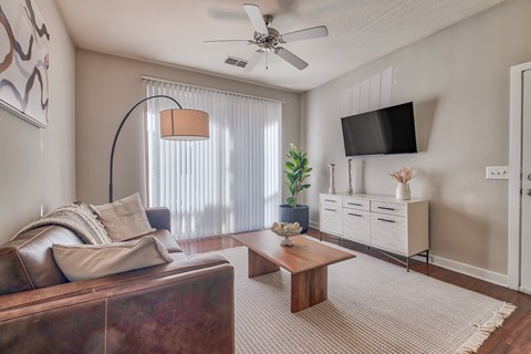 A living room with a brown couch, a wooden coffee table, a flat screen TV, and a ceiling fan.