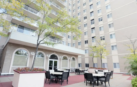 A patio with tables and chairs is surrounded by a building.