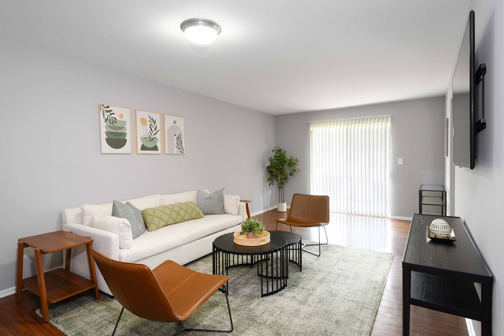 A living room with a white couch, a brown chair, a black table, and a television on the wall.