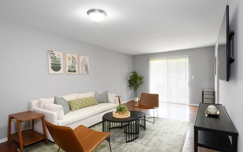 A living room with a white couch, a brown chair, a black table, and a flat-screen TV mounted on the wall.