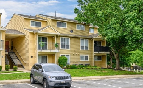 A silver SUV is parked in a parking lot in front of a yellow apartment building.