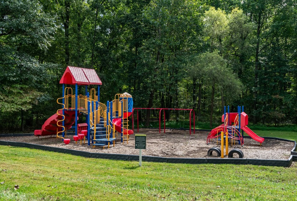 A playground with a red and yellow slide and a red and blue swing set at Park at Winterset Apartments, Owings Mills, MD