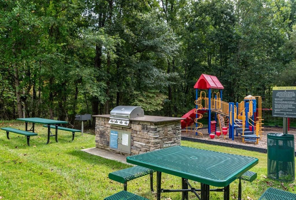 A playground with a slide, swings, and a picnic table is surrounded by trees at Park at Winterset Apartments, Owings Mills 21117