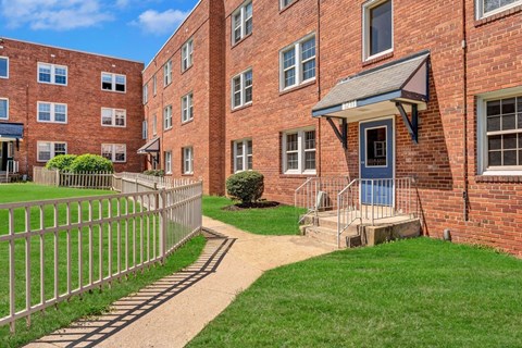 A red brick building with a small porch and a metal fence at Highland Ridge Apartments, Capitol Heights 20743