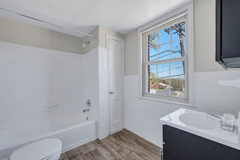A bathroom with a white toilet, a white sink, and a window with a view of the outdoors at Highland Ridge Apartments, Capitol Heights
