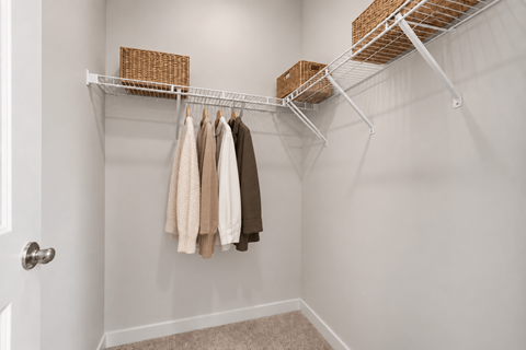 A white closet with clothes hanging on a rail.