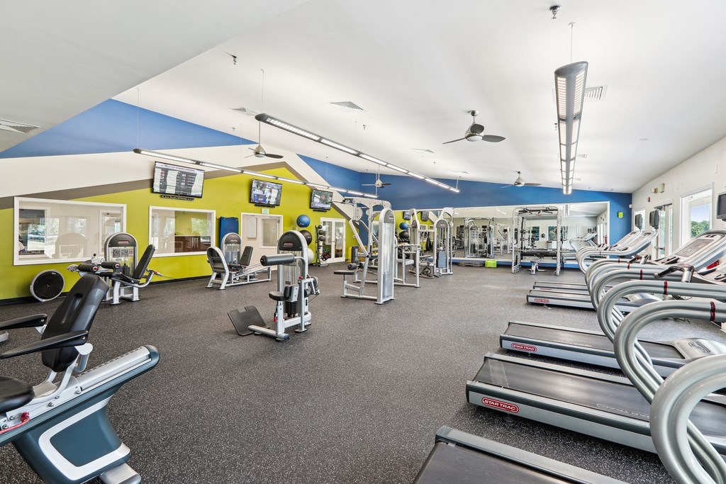 a gym with cardio equipment and weights on the floor and a yellow and blue wall at Villages at Morgan Metro, Landover, 20785