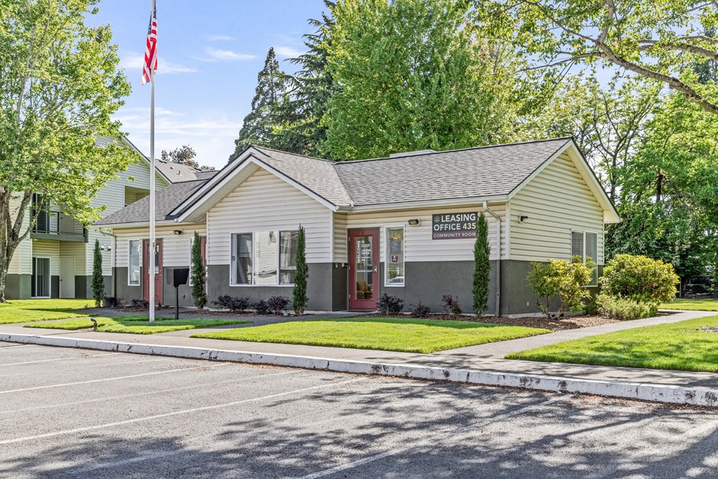 A building with a sign that says "LEASING OFFICE" is surrounded by trees and has a flagpole with an American flag in front of it.