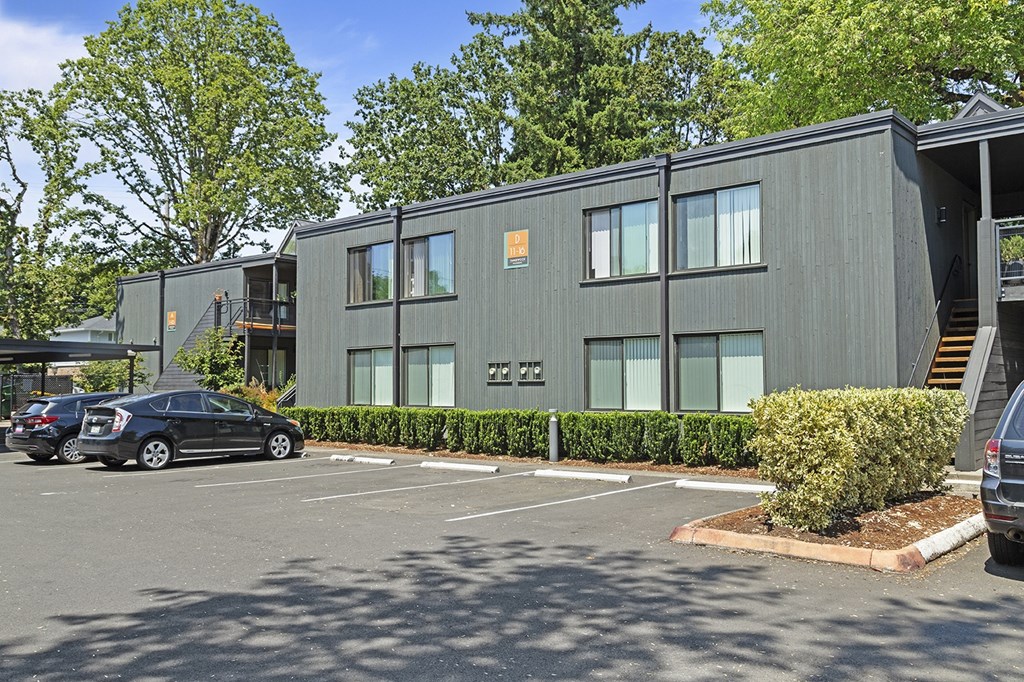 A grey building with a parking lot in front of it.