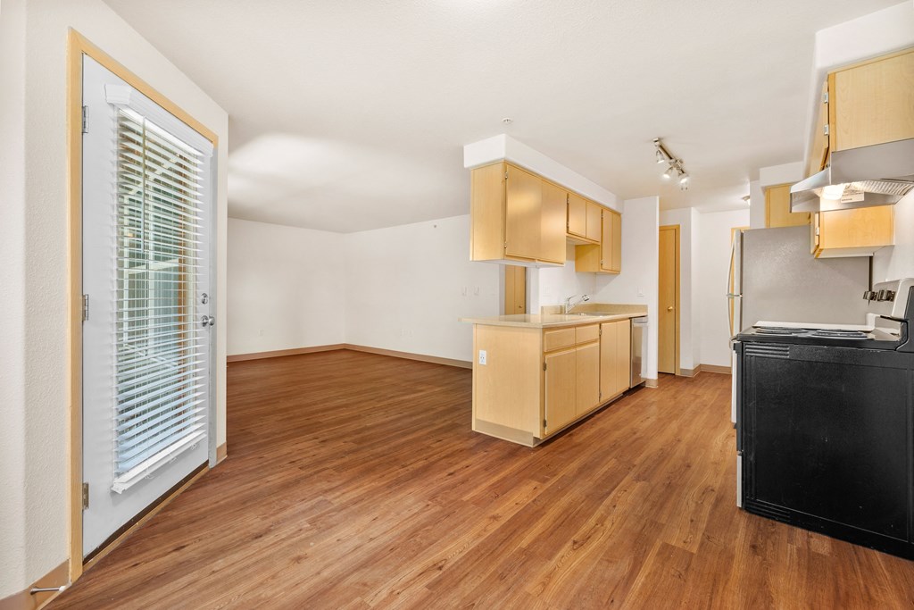 an empty living room and kitchen with wood flooring and a door to the kitchen