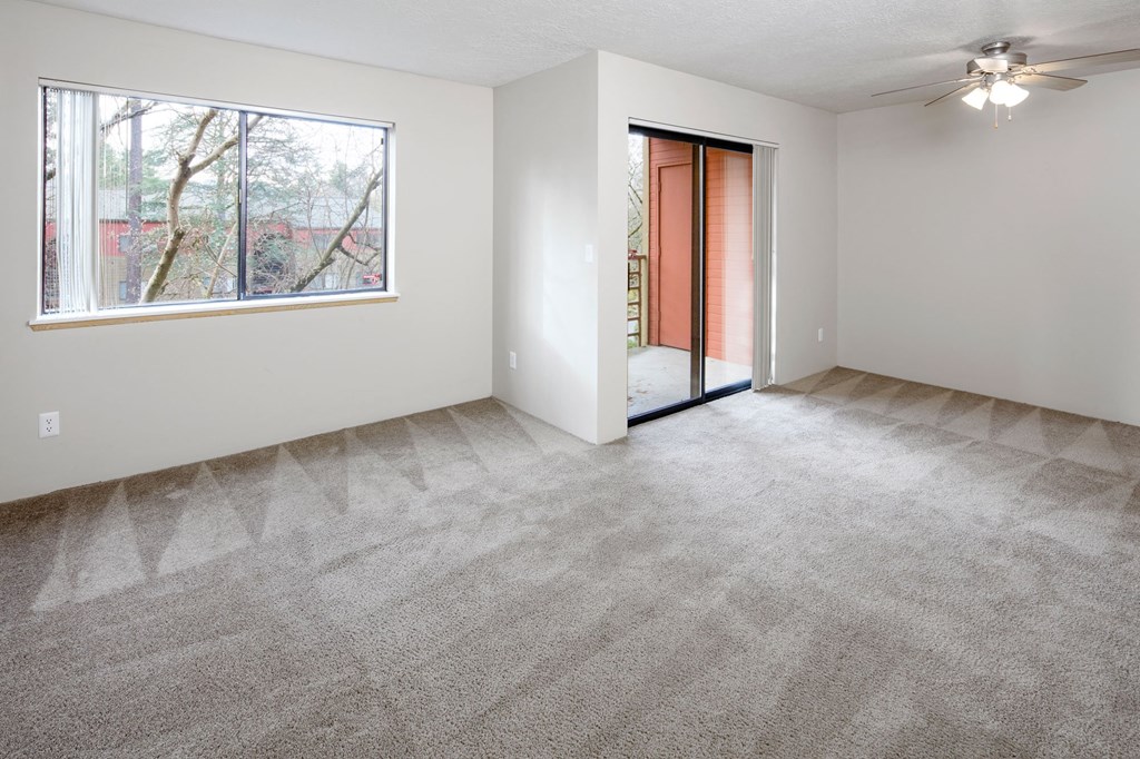 an empty living room with a large window and a ceiling fan