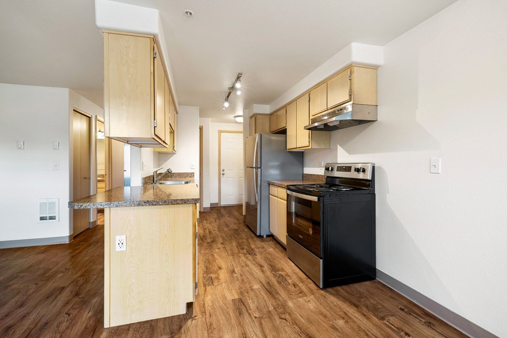 an empty kitchen with wood flooring and a black stove and refrigerator