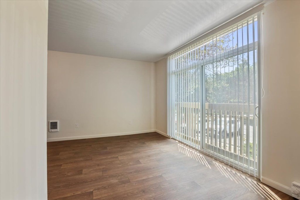 A room with wooden flooring and a sliding glass door leading to a balcony.