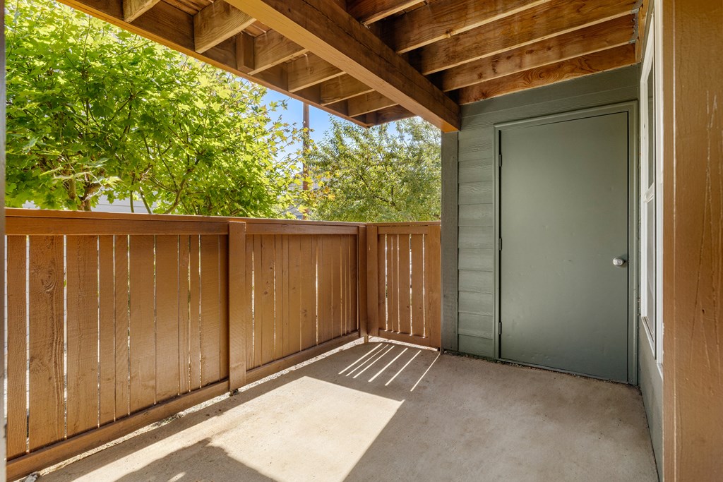 a covered deck with a privacy fence and a door to a balcony