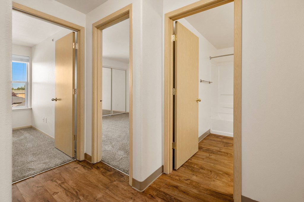 a living room with three doors and a hallway to a bedroom