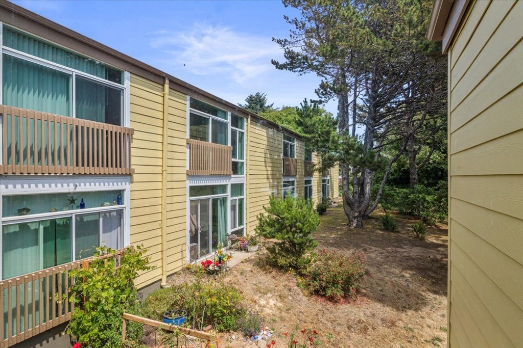 A view of a balcony with a railing and a small garden in front of a yellow building.