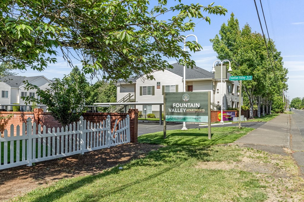 A sign for Fountain Valley Apartments stands in front of a white picket fence.