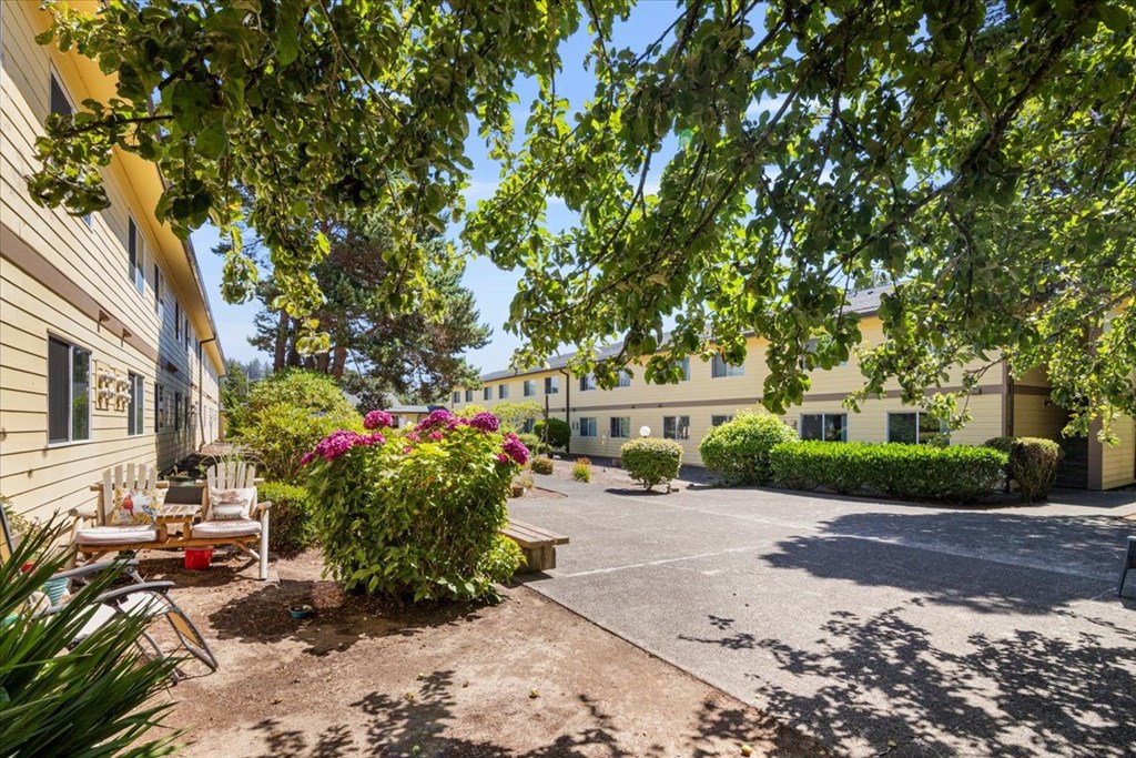A sunny day at a residential complex with a parking lot and greenery.
